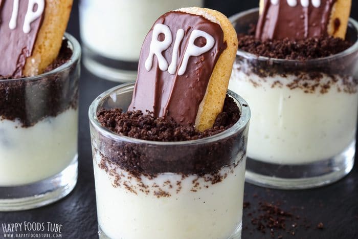 Mini graveyard dessert cups with Oreo “soil” and ladyfinger gravestones in clear glasses.
