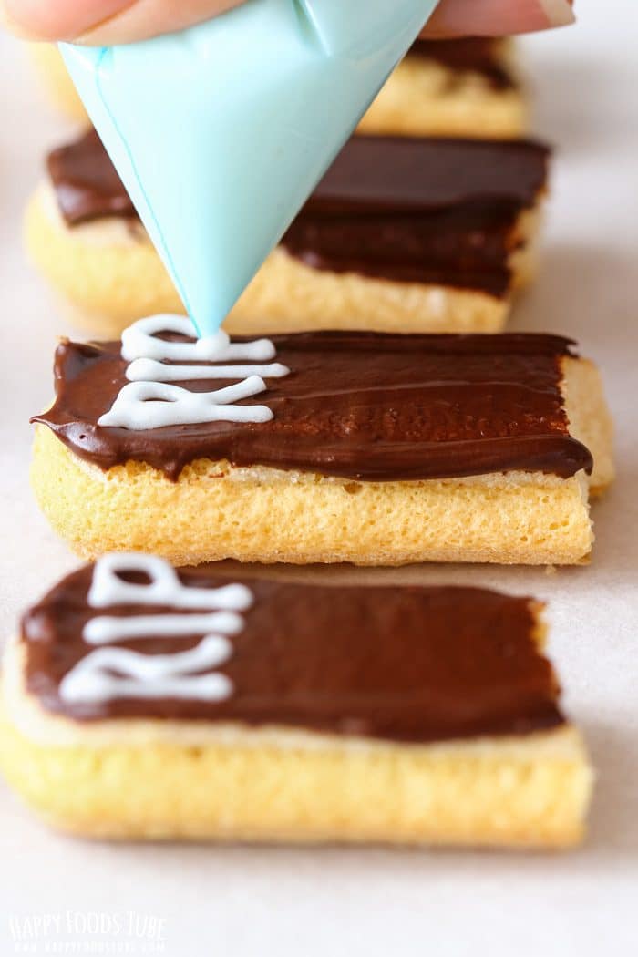 Piping white “RIP” letters onto chocolate-covered ladyfingers using royal icing.