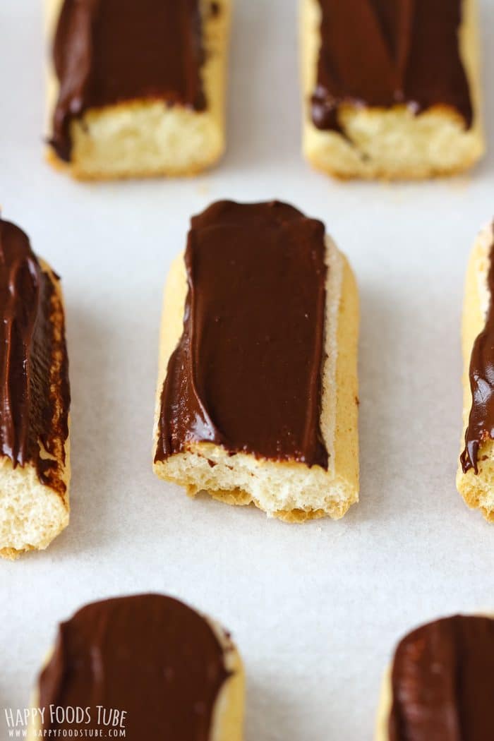 Chocolate-coated ladyfingers on parchment paper setting before decoration.