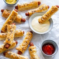 Hot dogs in a puff pastry with seeds, served with mustard, garlic sauce and ketchup.