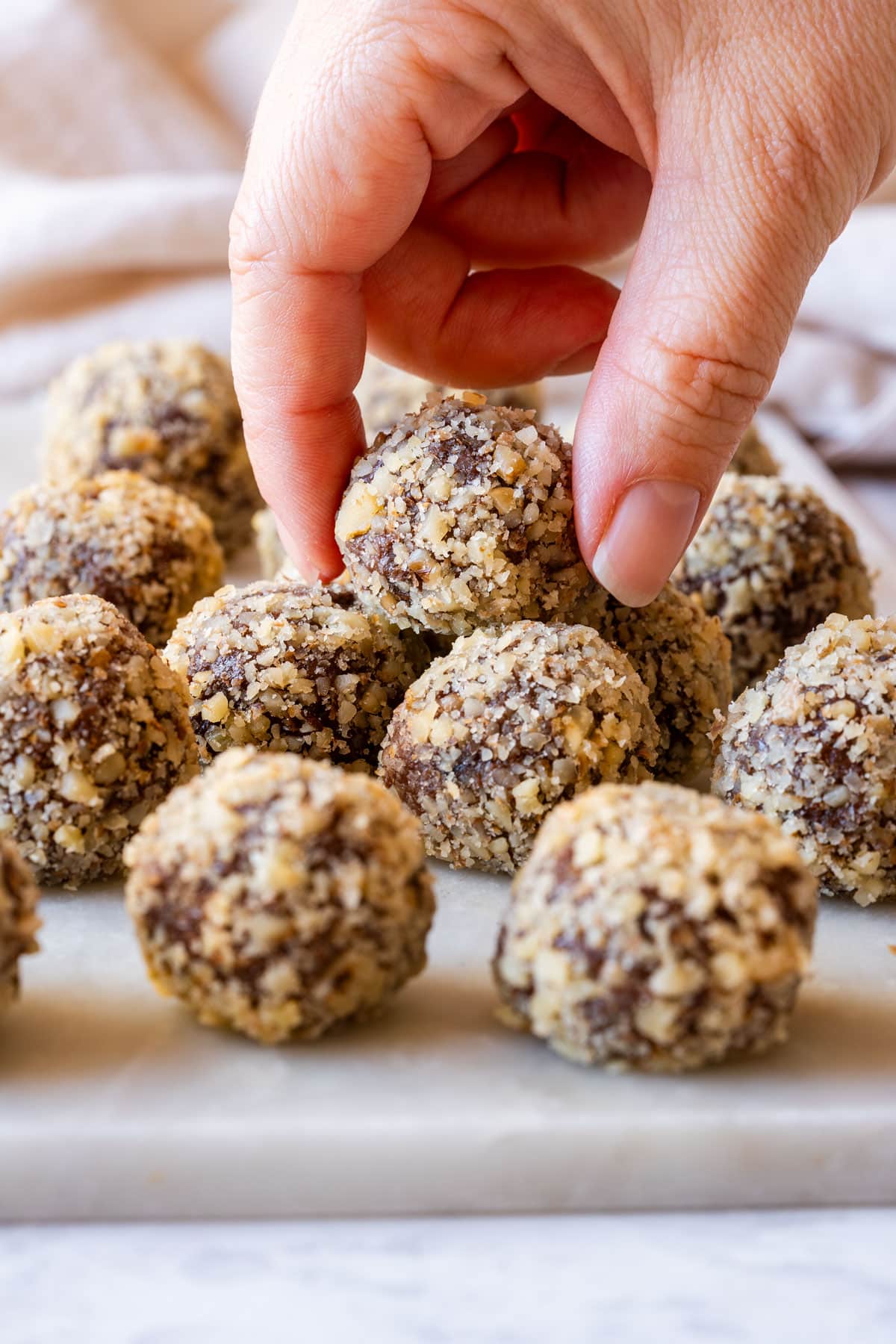 Hand picking up a walnut-coated chocolate truffle from a tray.