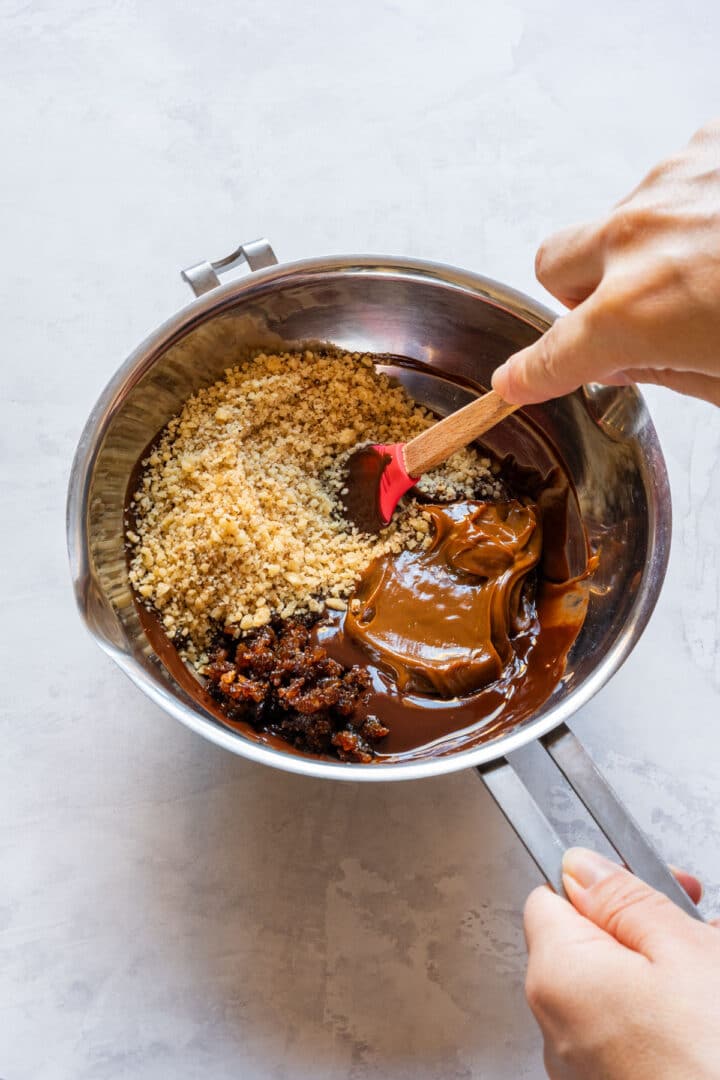 Mixing melted chocolate, dulce de leche, chopped walnuts, and raisins in a bowl.