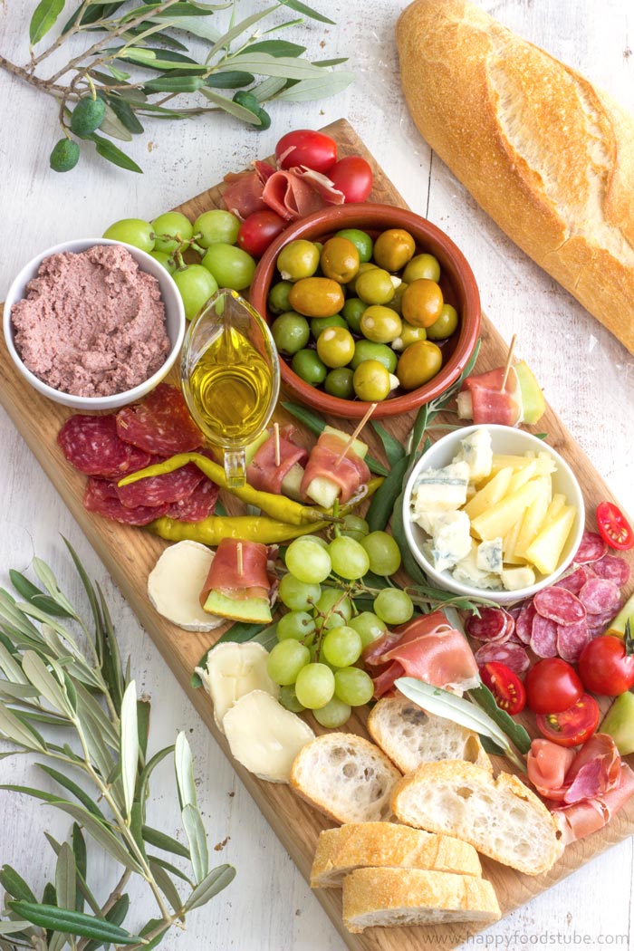 Mediterranean style antipasto platter with cheese, cured meat, olives, fruit and bread slices.