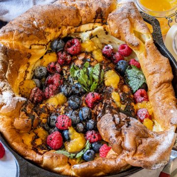 German pancakes (Dutch baby pancake) in a cast iron skillet with berries, lemon curd and powdered sugar.
