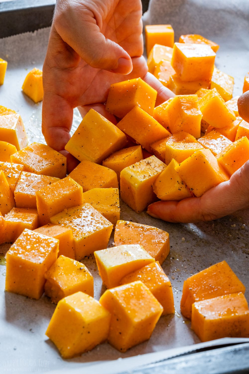 Tossing butternut squash cubes with olive oil.