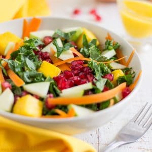 Bowl of kale salad with apple, mango, carrot and pomegranate served with mango dressing.