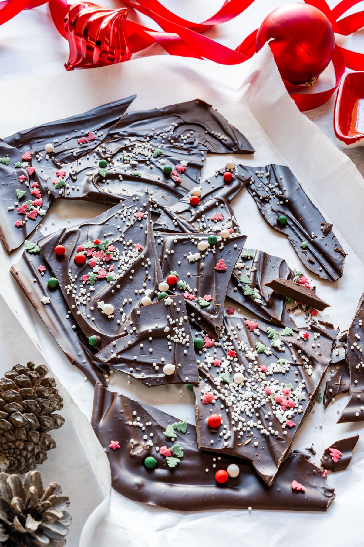 Dark chocolate Christmas bark with red, green and white sprinkles on parchment, styled with ribbon and ornaments.