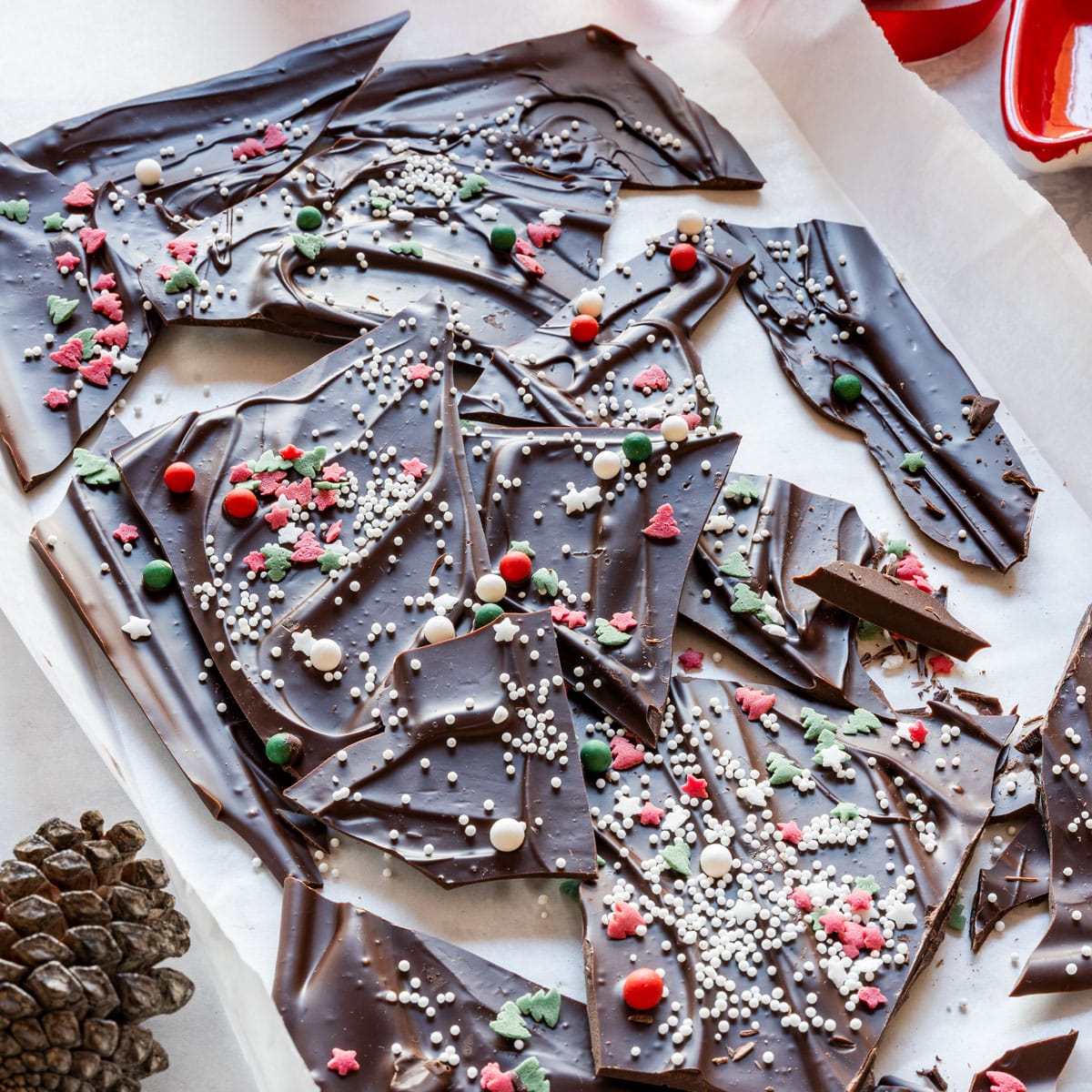 Overhead Christmas chocolate bark shards with red, green and white sprinkles on parchment.