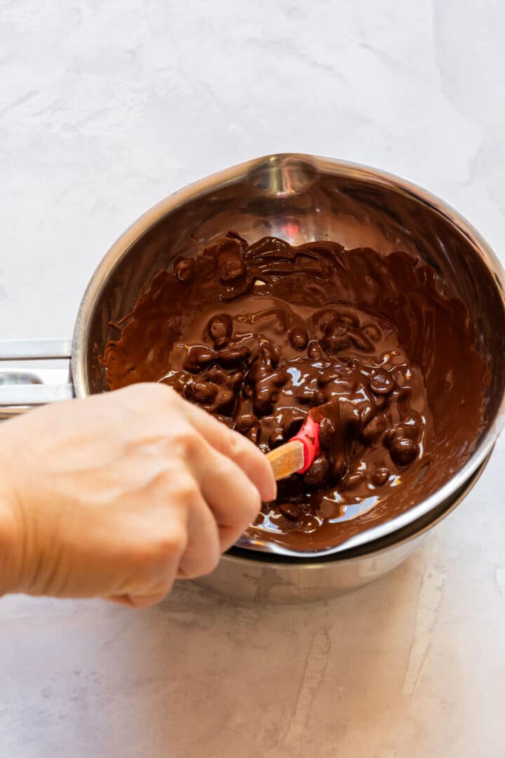 Tempering melted chocolate in a bowl over simmering water, stirring until smooth and glossy.