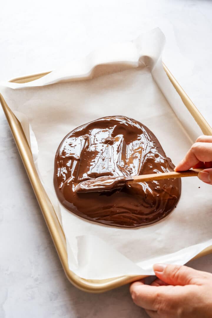 Spreading melted chocolate onto a parchment-lined baking sheet with a spatula.