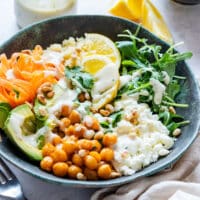 Homemade Mediterranean bowl with chickpeas, avocado, carrot ribbons, arugula, lemon slices and lemon tahini dressing.