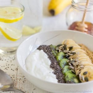 Fruit and yogurt breakfast bowl with banana, kiwi, chia seeds and sunflower seeds served with honey.