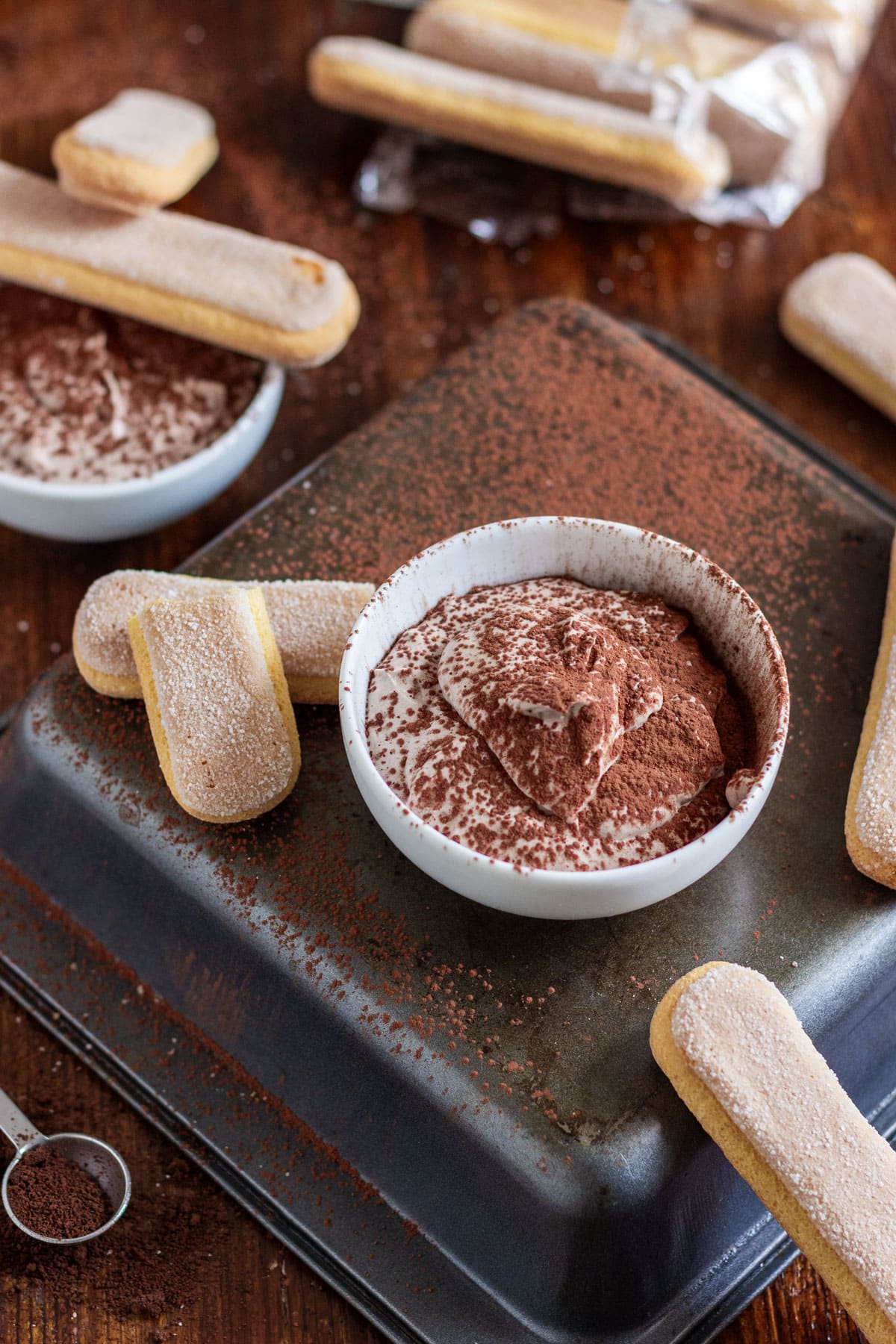 Ladyfingers and a bowl of tiramisu dip dusted with cocoa powder.