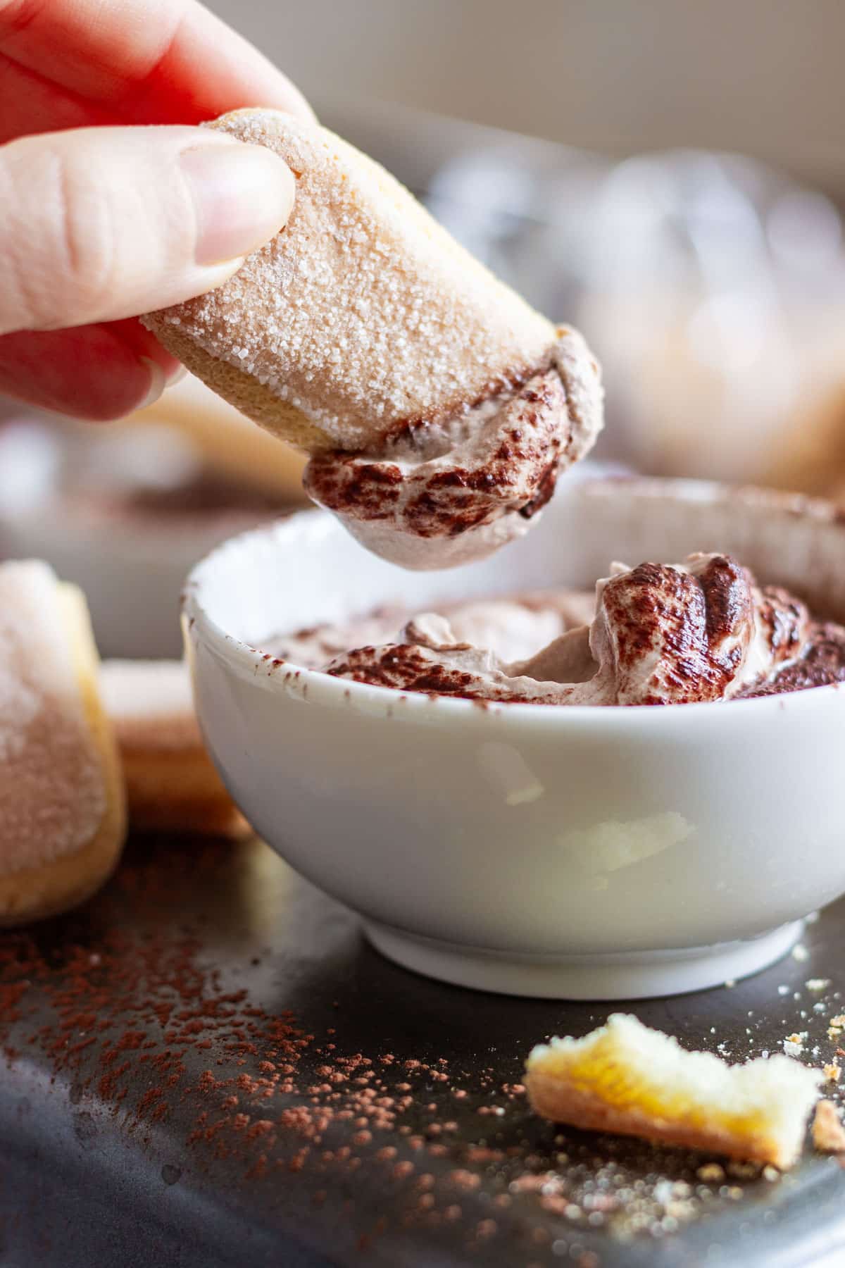 A hand dips a ladyfinger into a bowl of creamy tiramisu sweet dip.