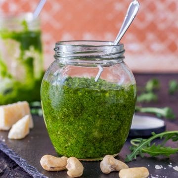 Arugula pesto in a glass jar with cashews and Parmesan on the side.