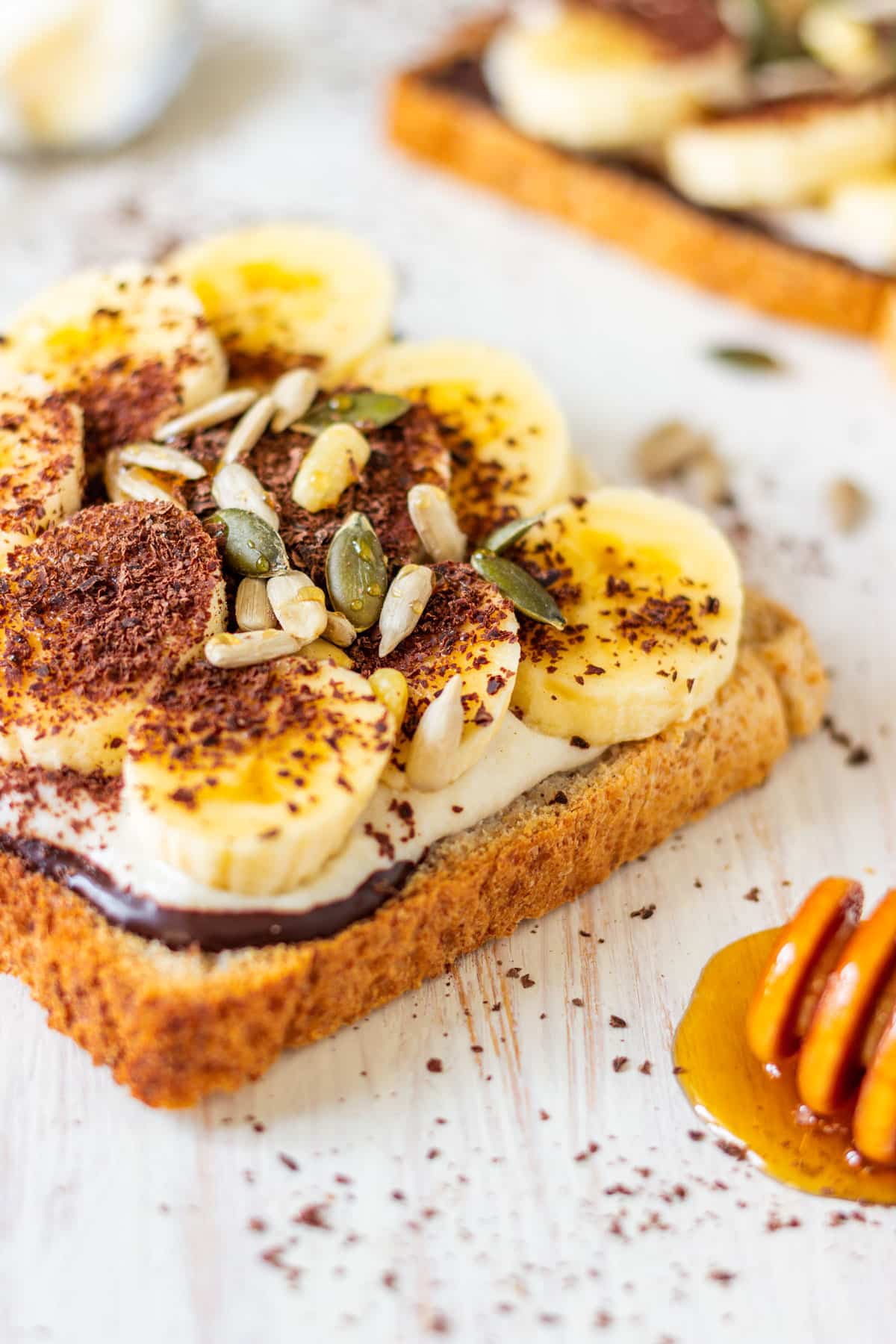 A slice of breakfast toast with banana slices, melted chocolate, ricotta, seeds and honey.