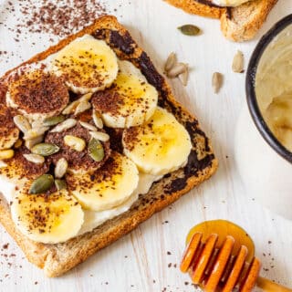 Breakfast banana toast with toppings, next to a cup and honey dipper.