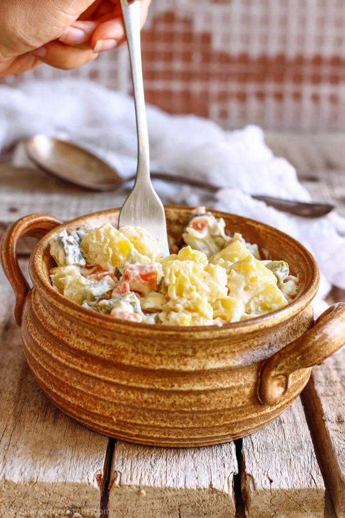 Eating potato salad with dill pickles with a fork.