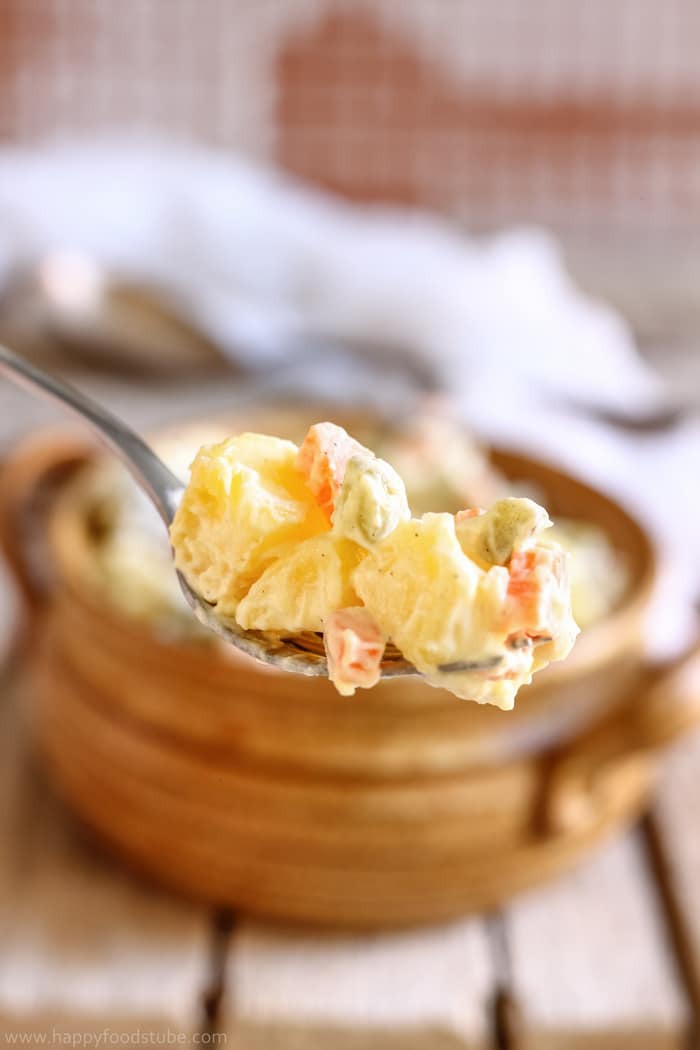 Closeup of potato salad on fork with dill pickle and carrot.