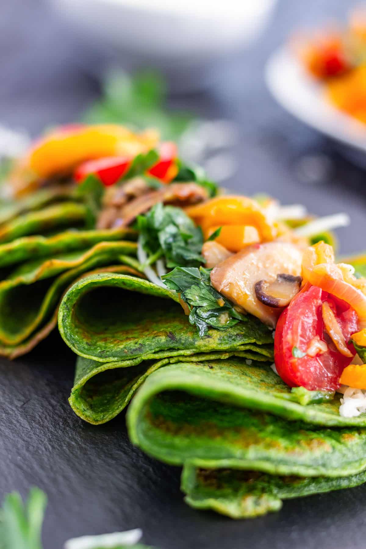Close-up of spinach crepes folded and topped with sauteed mushrooms, cherry tomatoes, bell peppers and fresh herbs.