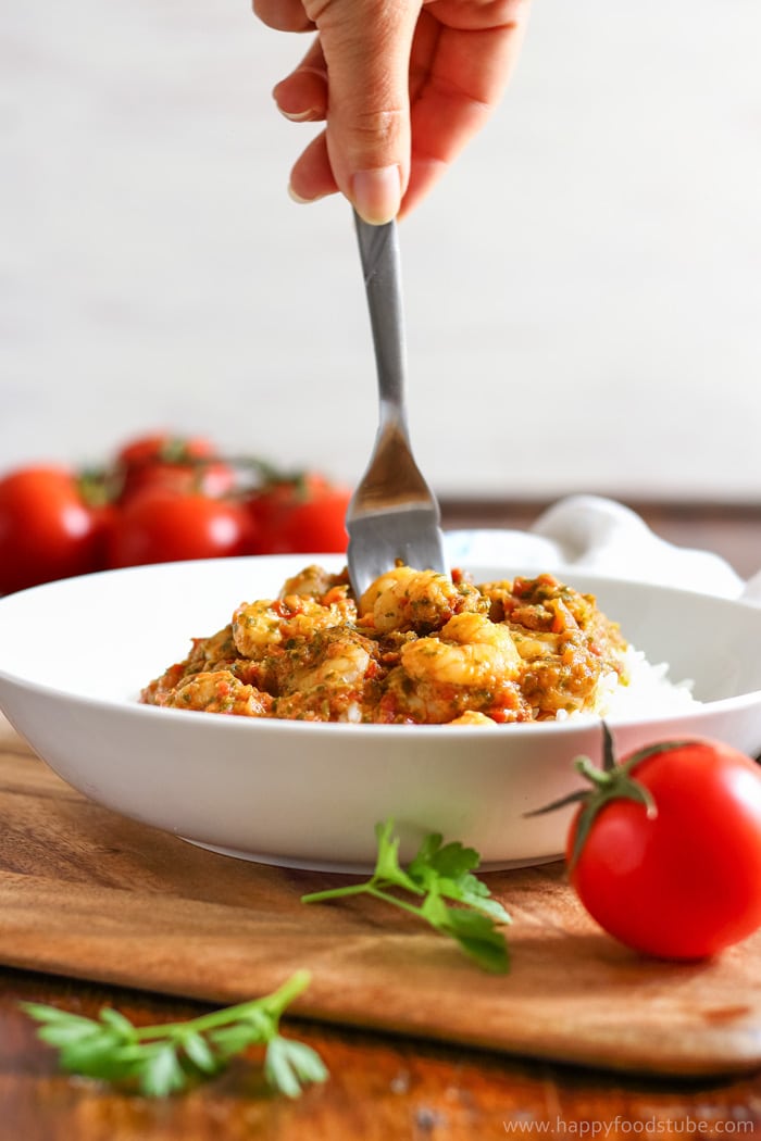 Shrimp in tomato sauce over rice, with tomatoes and a fork on a wooden board.