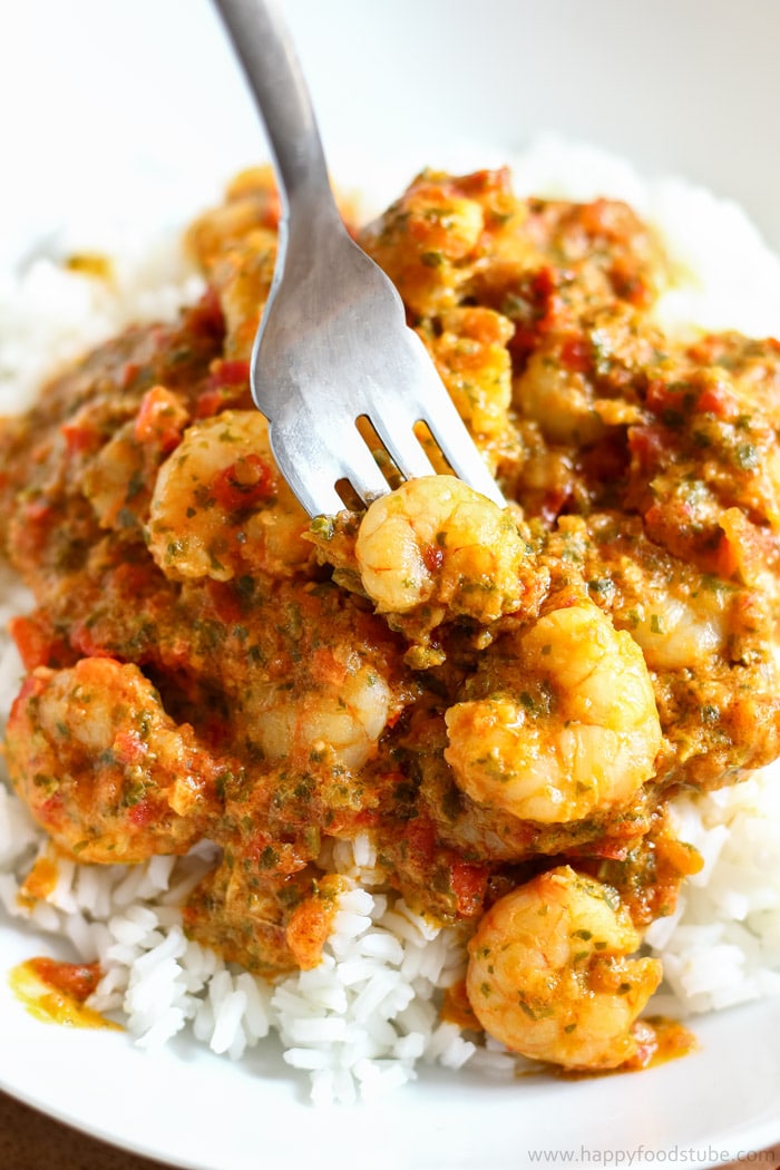 A fork is picking up shrimp covered in a tomato salsa sauce, served over white rice.