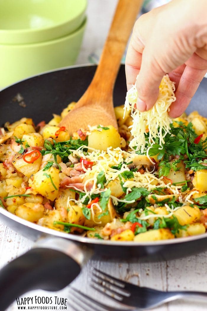 Hand sprinkling grated cheese over pan fried breakfast potatoes.