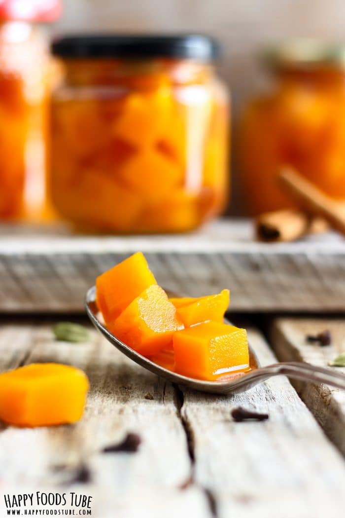 Pickled Pumpkin Photo Spoonful of spiced pumpkin cubes in front of small glass jars on a wooden board.