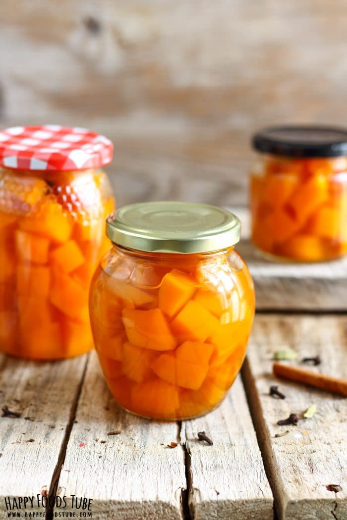 Pickled Pumpkin Pic Jar filled with pumpkin cubes in sweet–sour brine on a wooden surface, cinnamon stick and clove on the table.