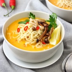 Thai-style pumpkin soup with noodles and mushrooms, lemon wedge on the side.