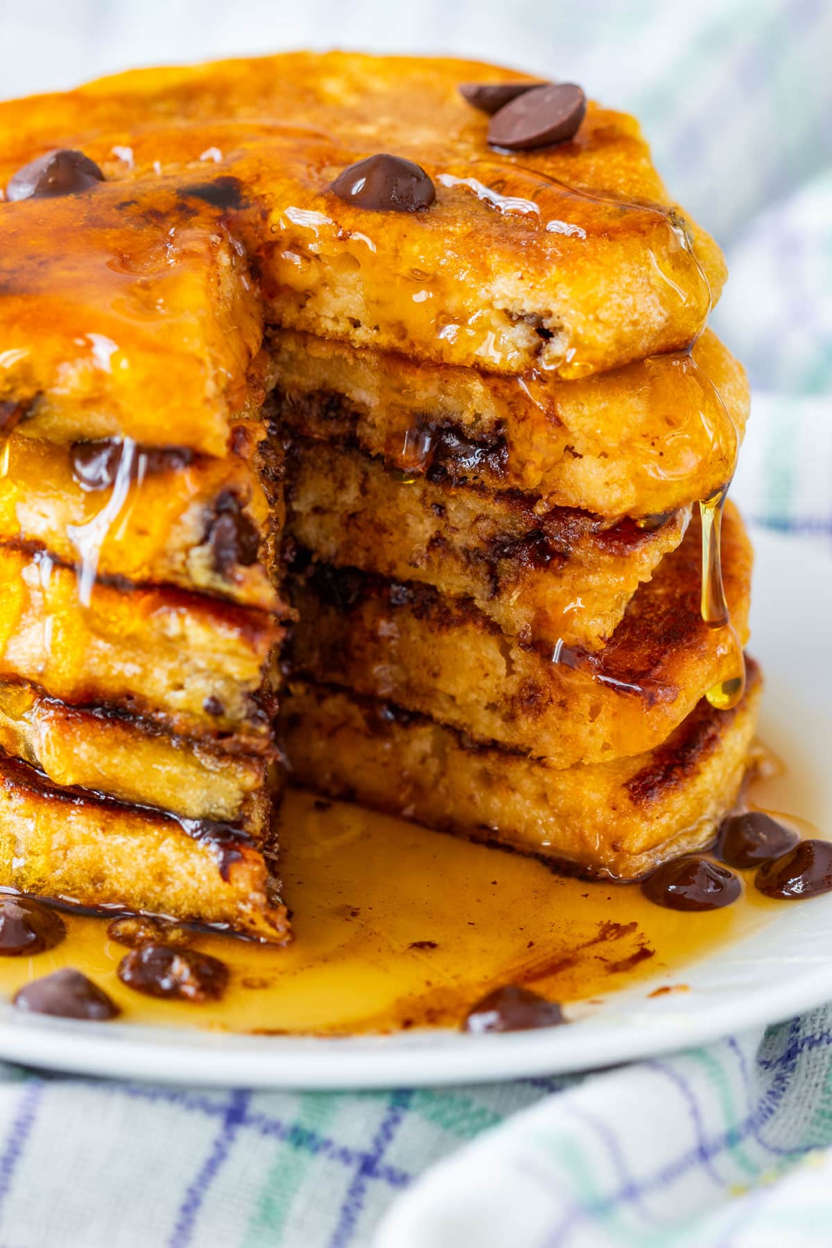 A stack of sweet potato pancakes with chocolate chips and syrup dripping down, partially cut to show the inside.