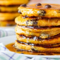 A stack of sweet potato pancakes drizzled with syrup on a white plate.