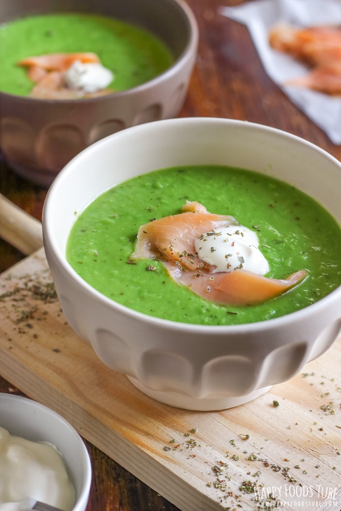 Bowl of green pea soup topped with sour cream and tiny slice of smoked salmon