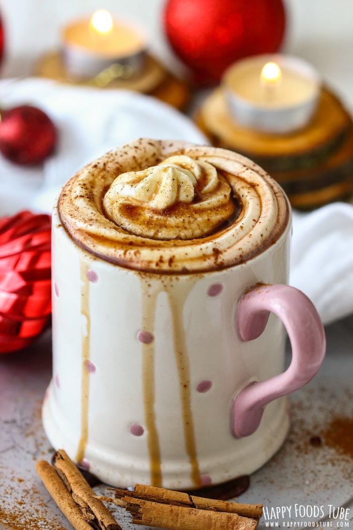 A festive hot chocolate with whipped cream and cinnamon, surrounded by candles and Christmas decorations.