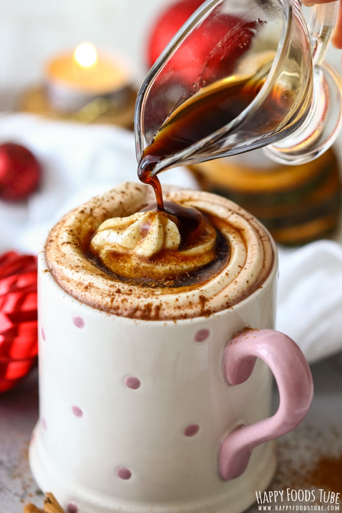 A close-up of a mug with whipped cream and gingerbread syrup being poured, creating a cozy, festive drink.