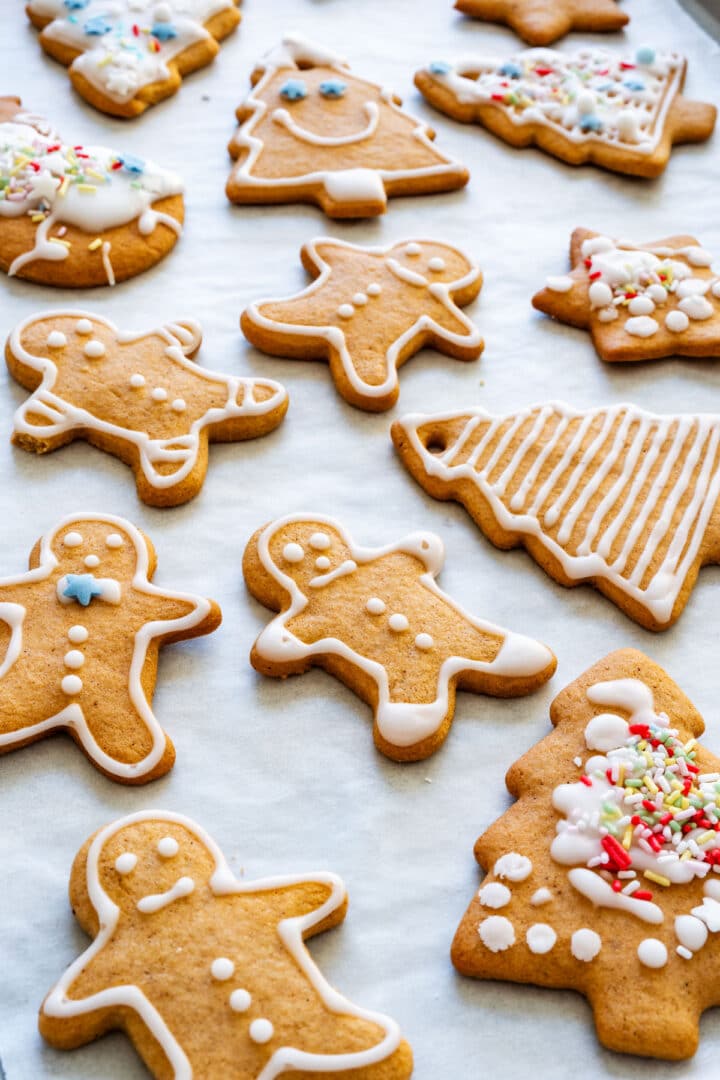 Honey gingerbread men and tree cookies decorated with white icing and sprinkles on parchment paper.