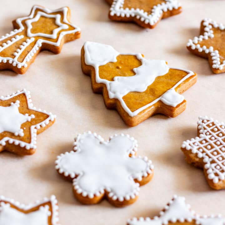 Honey gingerbread cookies without molasses decorated with white royal icing in star and tree shapes on baking paper.