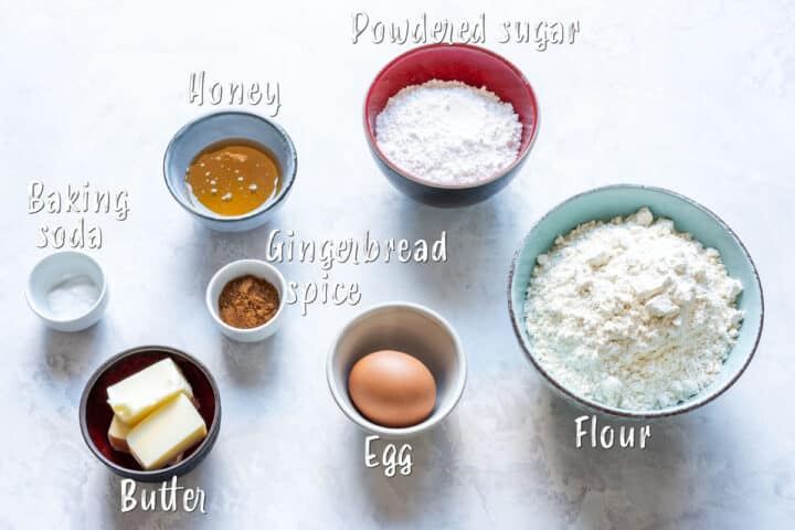 Ingredients for honey gingerbread cookies laid out in bowls, including flour, sugar, honey and spices.