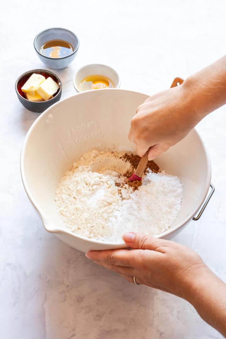 Mixing dry ingredients for gingerbread cookie dough in a large white bowl with a spatula.
