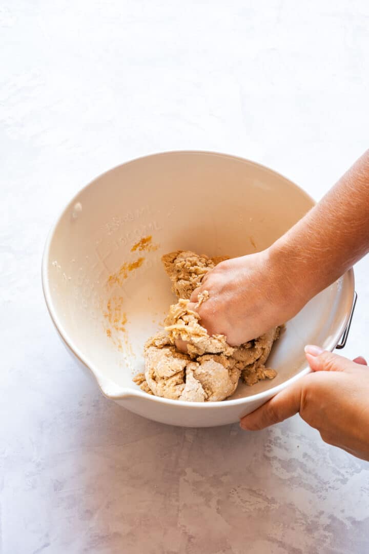 Kneading gingerbread dough by hand in a mixing bowl until it starts to come together.