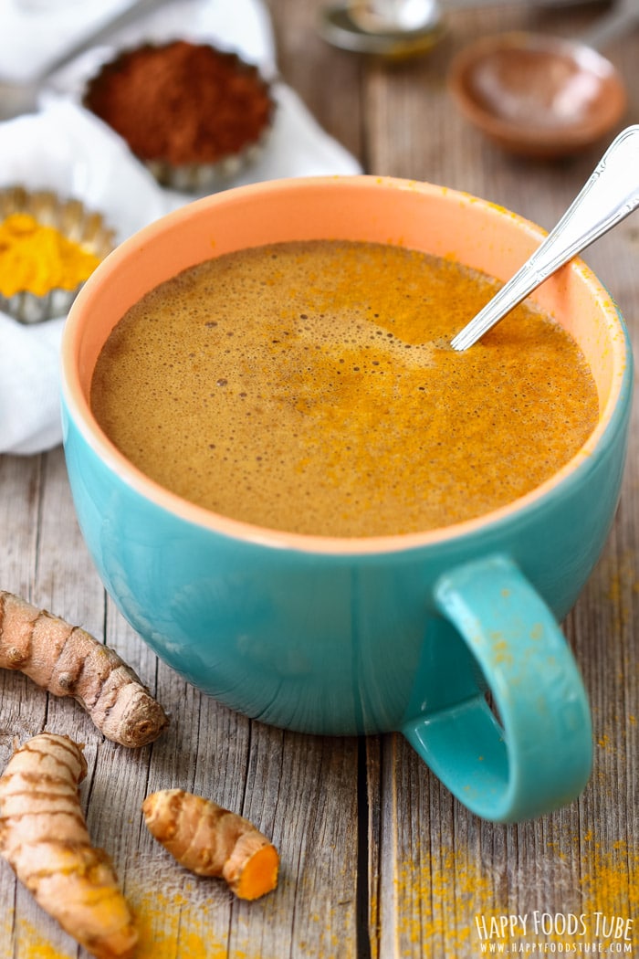 A large mug of golden homemade hot chocolate with turmeric, sitting on a rustic wooden table.