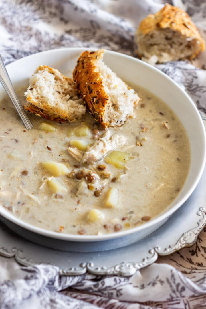 Creamy instant pot chicken lentil soup served with crusty seeded bread in a white bowl.