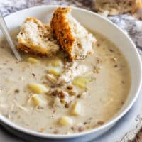 Bowl of creamy chicken and lentil soup with potatoes, served with seeded crusty bread.