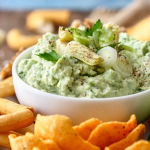 Green Artichoke Heart Dip on the white bowl with snacks