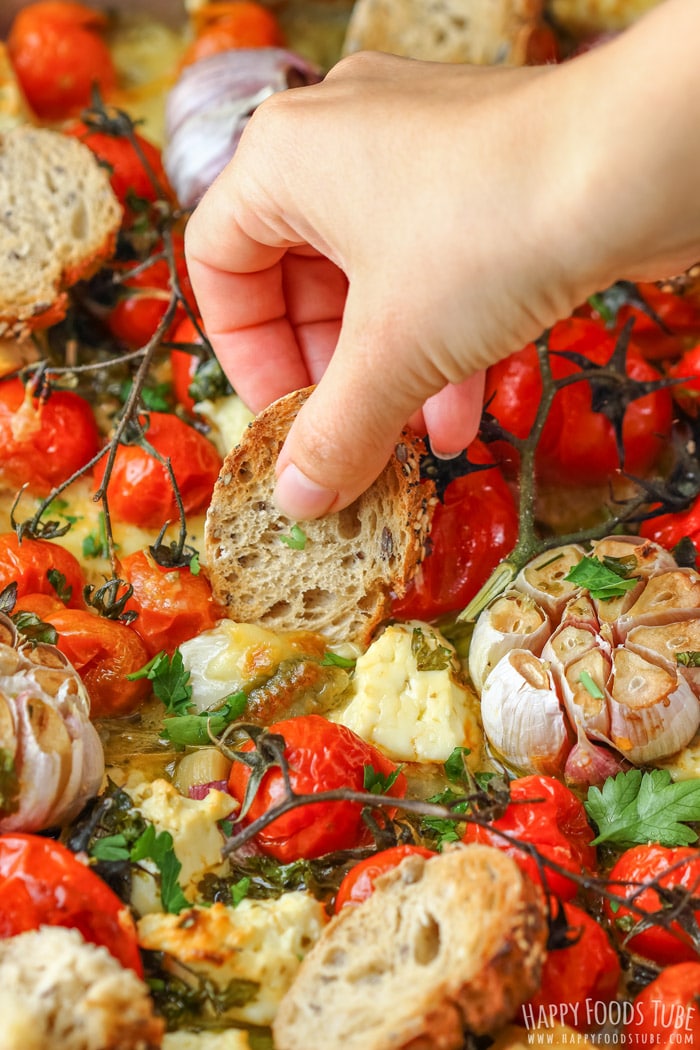 Dipping bread into Oven Roasted Cherry Tomatoes with Feta and Mozzarella