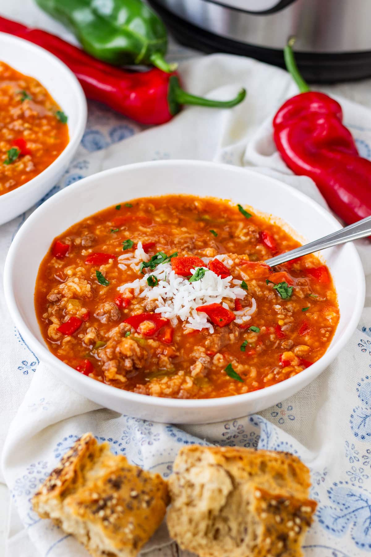 Bowl of stuffed pepper soup topped with rice, served with crusty bread, with fresh bell peppers and a pressure cooker in the background.
