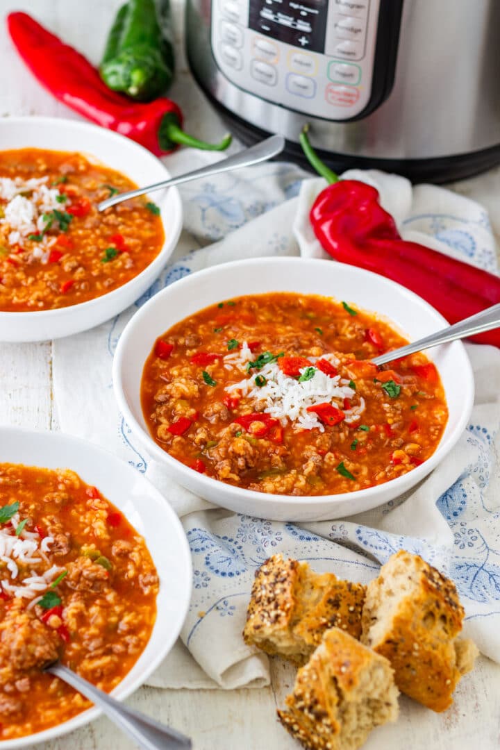 Stuffed pepper soup topped with rice, served with bread, fresh peppers, and an instant pot in the background.