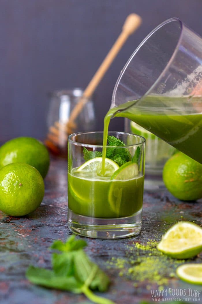 Pouring iced matcha tea into a glass with lime and mint.
