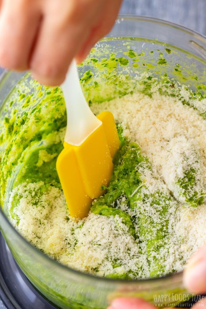 Stirring Parmesan into pesto in a food processor bowl.