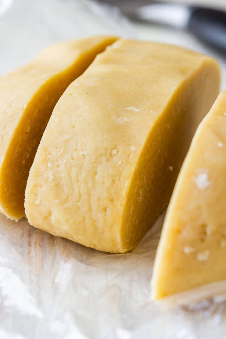 Log of Linzer cookie dough cut into pieces on plastic wrap, ready to be rolled out.